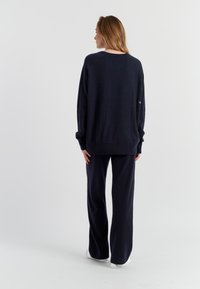 Maglione a maglia blu navy e pantaloni a gamba larga coordinati. Il maglione presenta un collo a giro e spalle scese; entrambi hanno una texture morbida.