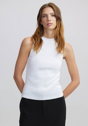 Haut sans manches blanc à côtes avec un col montant, présentant une coupe ajustée et une texture lisse, associé à un bas noir.