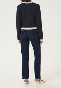 Marineblauer, verkürzter Pullover mit cremefarbenem Saum, kombiniert mit dunkelblauen Straight-Leg-Jeans. Neutrale Absatzschuhe; simples Design mit minimalen Details.