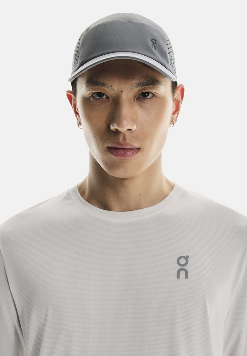 Gray cap with perforated sides, white trim, and a logo, worn with a long-sleeve white shirt featuring a small gray logo on the chest.