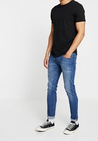 Camiseta negra de manga corta con puntos en relieve, combinada con vaqueros ajustados azul y zapatillas negras con suelas y cordones blancos.