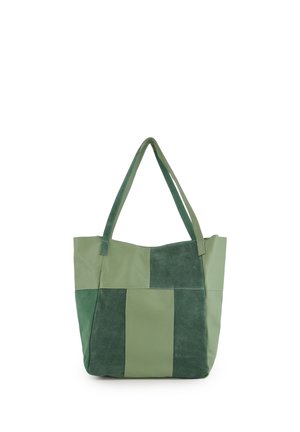 Grøn patchwork-tote-taske med to håndtag, der kombinerer ruskind og glatte læderpaneler, står oprejst på en hvid baggrund.