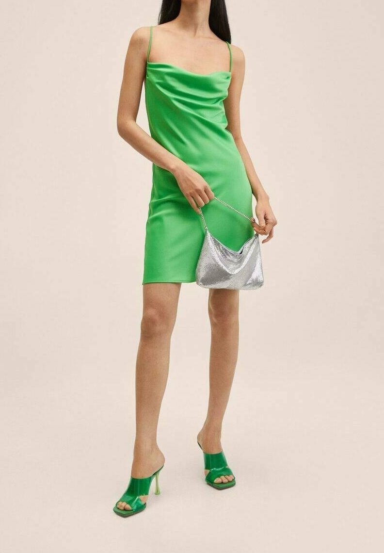 Robe mini en satin vert avec encolure drapée, associée à un sac à main métallique argenté et des sandales à talons ouverts vertes.