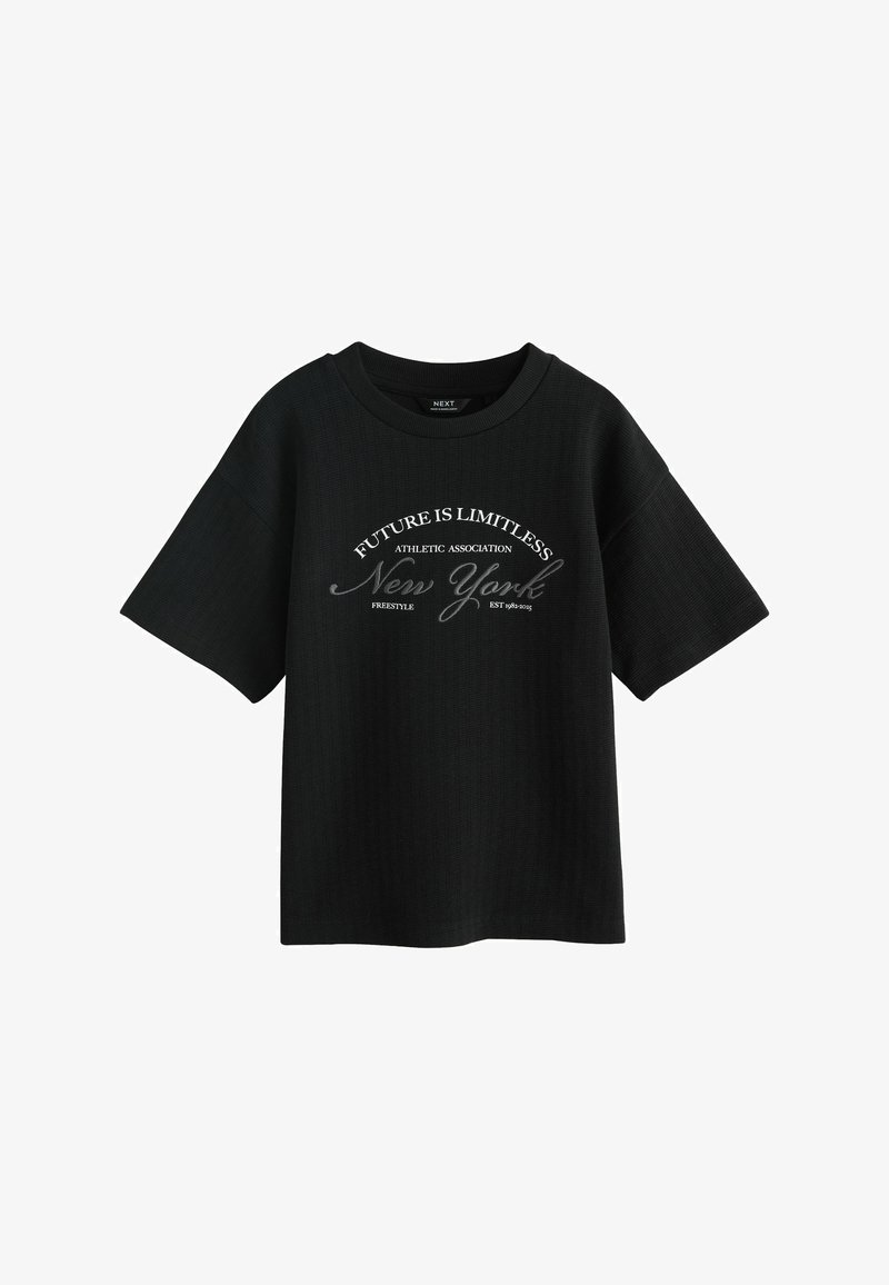 T-shirt noir à manches courtes avec texte blanc "FUTURE IS LIMITLESS," "Athletic Association," "New York" et "Freestyle Est 1982-2025" au devant.
