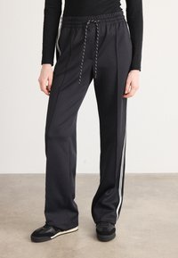 Pantalons de sport noirs en tissu texturé avec une taille élastique à cordon de serrage et des bandes latérales. Le design comprend une coupe décontractée et des jambes fuselées.