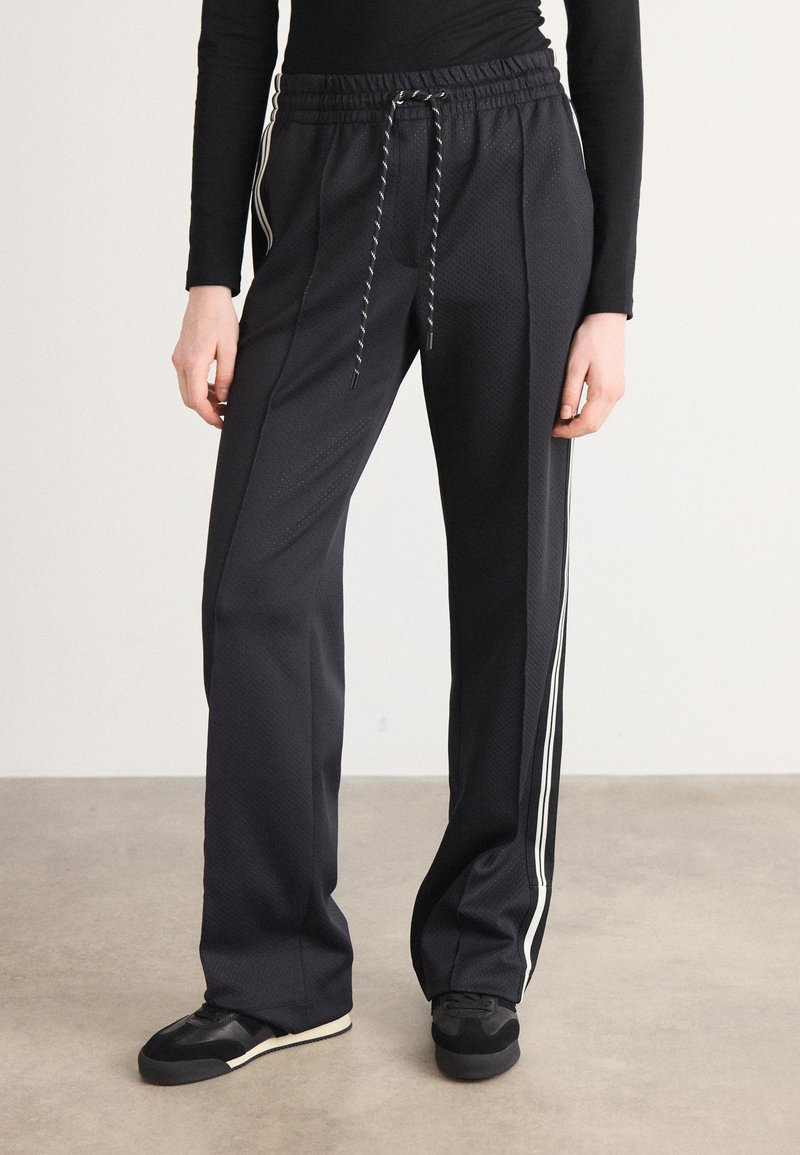 Pantalons de sport noirs en tissu texturé avec une taille élastique à cordon de serrage et des bandes latérales. Le design comprend une coupe décontractée et des jambes fuselées.