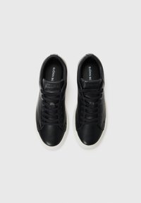 Svarte lær-sneakers med jevn tekstur, rund tå og hvite gummisåler. Har svarte snører og fremtredende merkevarelogo på tungen.
