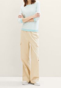 Ljusblå och vit randig långärmad topp med rund hals, kombinerad med beige cargobyxor med sidofickor och avslappnad passform. Vita sneakers.