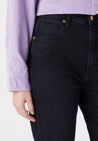 Czarne dżinsy o wysokim stanie z klasycznym pięciopocketowym wzorem, z miedzianymi nitami. Połączone z fioletową, teksturowaną bluzką w prążki.