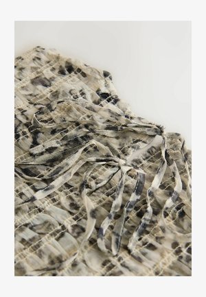 Kerge, läbipaistev beežist kangast top, millel on mustad abstraktsed mustrid. Kaeluses on nöörid ja kogu tükil on tekstuuriga ruudustikuline kujundus.