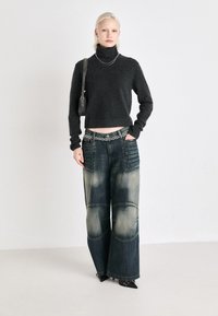 Suéter cinza de gola alta, design cropped, combinado com jeans de perna larga com remendos desbotados e bolsos texturizados. Sapatos de salto pretos e cinto de corrente.