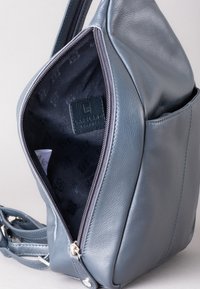 Gray leather handbag with a zip closure, featuring a smooth texture, external pocket, and branded interior lining. Adjustable strap included.