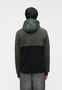 Φούτερ με κουκούλα σε σκούρο πράσινο και μαύρο. Απαλό υλικό φλις, σχεδιασμός με διαχωριστικά χρώματα, φουσκωτή κουκούλα και ριμπ μανσέτες. Άνετη casual εφαρμογή.