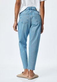 Ljust blå högmidjade jeans med en tapered passform, fransad fåll och två bakfickor. Materialet är denim med en slät yta.