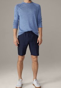 Chemise bleue à manches longues, col rond, coupe décontractée. Shorts marine arrivant aux genoux, taille avec cordon de serrage. Baskets blanches avec semelles en caoutchouc.