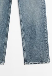 Blauwe spijkerbroeken met rechte pijpen en zichtbare stiksels op een witte achtergrond.