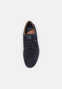 Zapato de ante azul marino con punta redonda, cordones planos y forro interior marrón. Presenta un sutil patrón texturizado y una plantilla con marca.