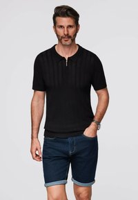 Black knit polo shirt with short sleeves, featuring a zip placket and ribbed texture, paired with rolled denim shorts.