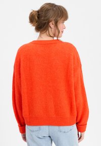 Prevelik svetlo oranžen pulover z mehkimi teksturami, rebrastimi manšetami in robom ter širokim, okroglim izrezom. Zasnovan za sproščen kroj.
