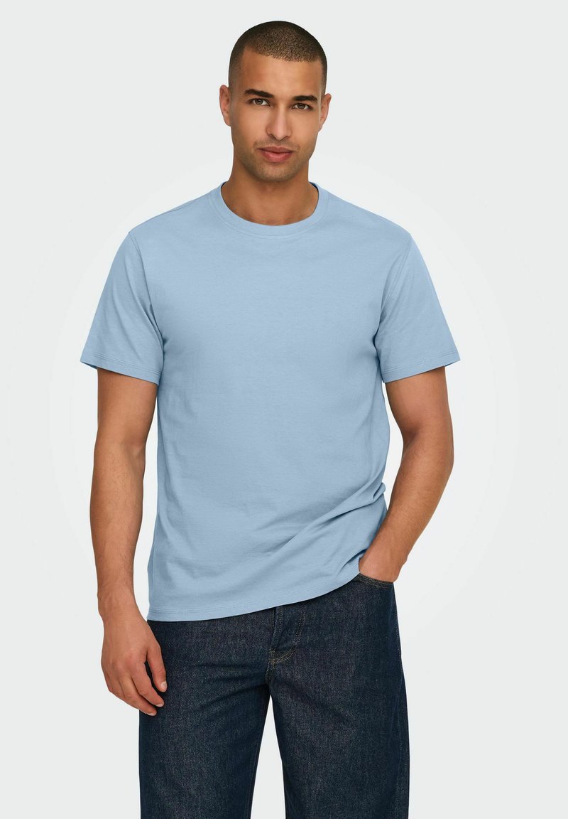 Helles blaues Baumwoll-T-Shirt mit Rundhalsausschnitt, kurzen Ärmeln und lockerer Passform, kombiniert mit dunklen Jeans.