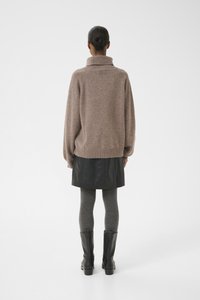 Suéter marrón de gran tamaño con cuello alto, falda corta de cuero negro, medias grises con textura y botas negras de tacón.