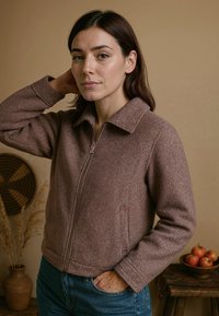 Bruine, gestructureerde jas met een rits aan de voorkant en een kraag. Heeft zijzakken en lange mouwen. Gekocht met blauwe jeans. Eenvoudig ontwerp.