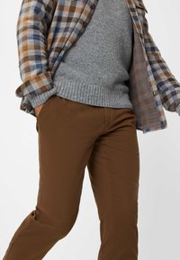 Pantaloni di cotone marroni abbinati a un maglione grigio e una camicia a scacchi con colori blu, marrone e crema. Texture liscia.