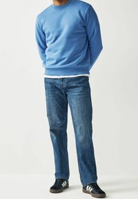 Sweat-shirt bleu clair, jean bleu denim, et baskets noires avec des rayures blanches, présentés sur un fond neutre.