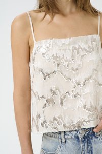 Sleeveless cream top featuring a textured pattern with metallic accents and sequins. Worn with light blue denim shorts.