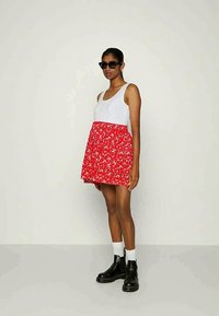 Vestido floral vermelho com parte superior branca, feito de tecido leve. A modelo usa óculos de sol pretos e botas ankle pretas com meias brancas.