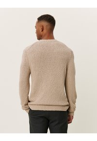 Suéter de textura beige con cuello redondo, puños y dobladillo acanalados. Presenta un ajuste holgado con un patrón visible en toda la tela.