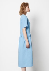 Lys blå kjole med korte ermer, rund halslinje, innsnevring i midjen og en sidelomme. Laget av teksturert stoff, knelengde design.
