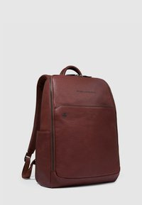 Zaino in pelle marrone dal design strutturato. Caratterizzato da una tasca frontale con zip, spallacci imbottiti e manico superiore per il trasporto. Marchio semplice.