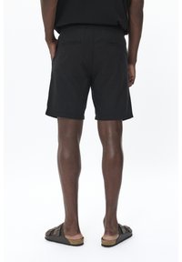 Black shorts with an elastic waistband, two back pockets, and a relaxed fit. Worn with brown sandals featuring a cork sole.