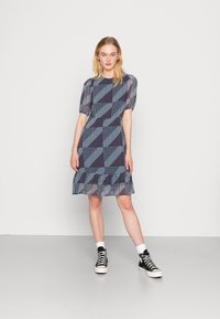 Vestido azul com padrão, com mangas curtas em puff, designs triangulares e de bolinhas, com bainha franzida, combinado com ténis pretos de cano alto.