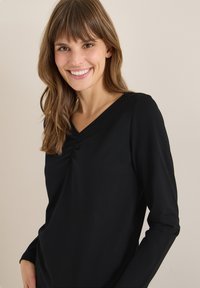 Maglietta nera a maniche lunghe con scollatura a V e dettagli arricciati sul petto, realizzata in un tessuto morbido, con una vestibilità morbida e una texture liscia.