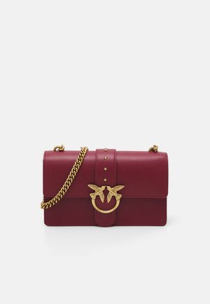 Sac à main en cuir rouge foncé avec une bandoulière chaîne en or et un fermoir doré présentant deux oiseaux se faisant face.