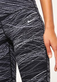 Černé a šedé legíny s vzorem vln, vyrobené z pružného materiálu. Maj�í šitý šev a malé logo Nike na stehně.