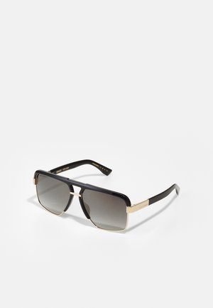 Lunettes de soleil noires avec des accents dorés, verres rectangulaires et finition brillante. Caractéristiques d'un pont en métal et de branches élégantes. Verres dégradés.