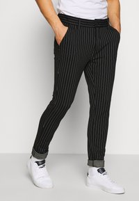 Černé pruhované kalhoty mají slim fit, boční kapsy a manžetový lem. Jsou skvěle zkombinovány s bílými teniskami pro ležérní vzhled.