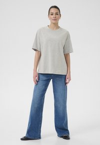 Light gray oversized t-shirt made of soft fabric, paired with wide-leg blue denim jeans. Model stands facing forward with a neutral background.