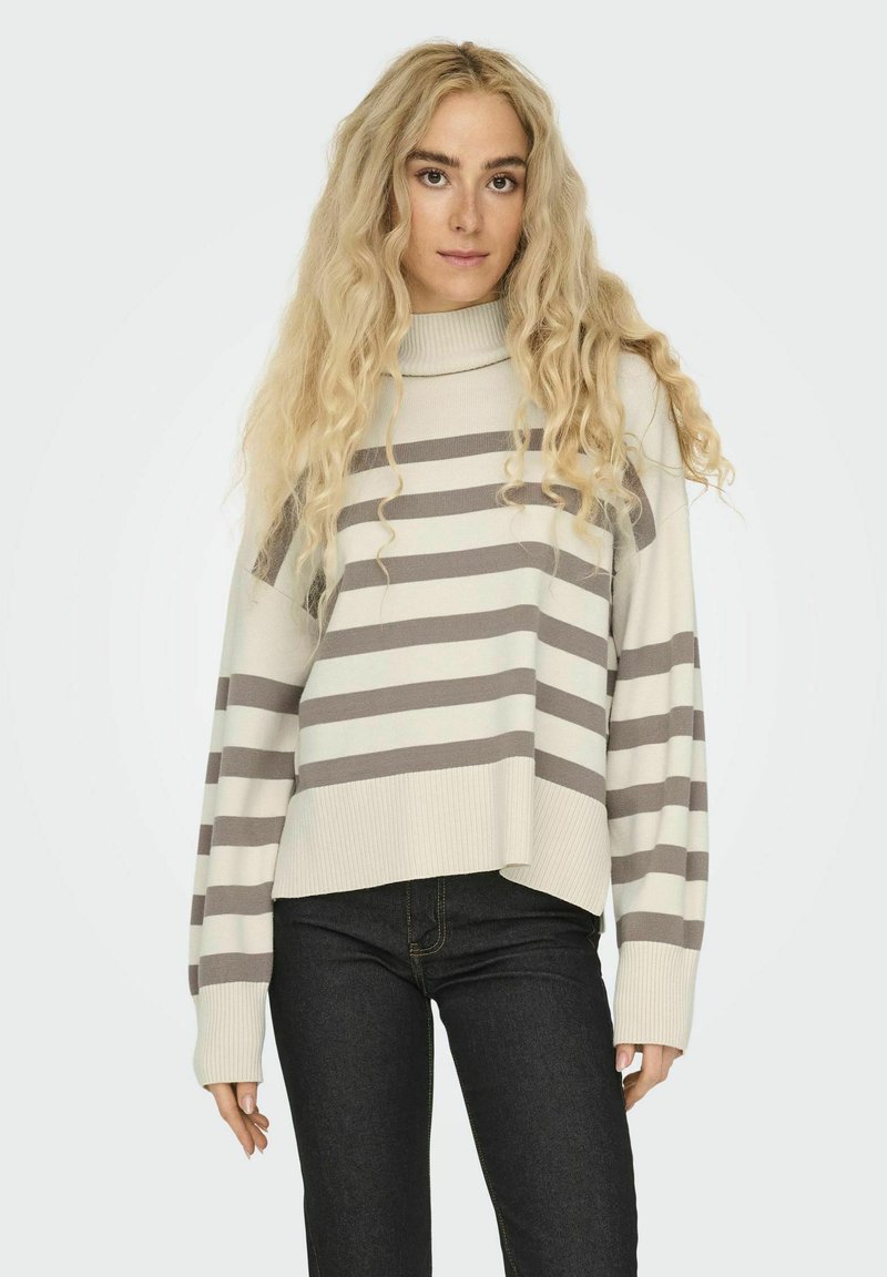 Pull rayé en crème et taupe, doté d'un col roulé et d'épaules tombantes. Ourlets et manches côtelés. Assorti avec un jean foncé.