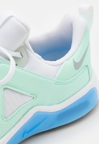 Light mint green sneaker with textured synthetic material, white mesh details, and blue rubber sole. Features gray logo and smooth accents.