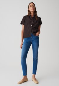 Chemise noire à manches courtes avec boutons, jean skinny bleu, et ballerines beiges. La chemise a une poche et une finition légèrement texturée.