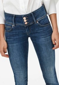 Slimmade jeans i mörkblå denim med hög midja och tre bronsknappar samt framfickor. Slät textur, klassisk design.