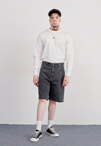 Pantalones cortos de mezclilla negros combinados con una camisa blanca de manga larga y zapatillas negras. Incluye pantalones cortos con dobladillo y detalles contrastantes en los accesorios.