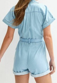 Denim romper vaaleansinisena, lyhyet hihat, vyöllä vyötäröllä, suuret hihansuut, rento istuvuus, sileä pinta, taka-näkymä.