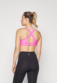 Rozā sporta krūšturis ar krustenisku aizmuguri, zem kura ir logotipa josla. Kombinēts ar augsto jostasvietu melniem leggings, gluda tekstūra.