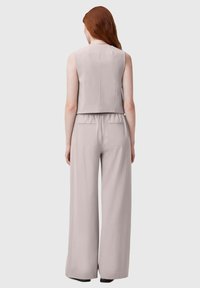 Giubbotto senza maniche grigio chiaro con scollatura alta, corpetto su misura, vita elasticizzata e pantaloni a gamba larga. Tessuto liscio e tasche discrete.