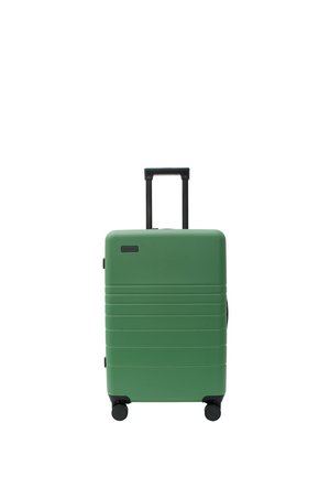 Grüner Hartschalenkoffer mit ausgezogenem Teleskopgriff und vier schwarzen Spinner-Rollen, stehend auf weißem Hintergrund.